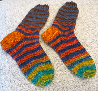 Bright, stripey hand-knit socks socks with contrasting orange heels.